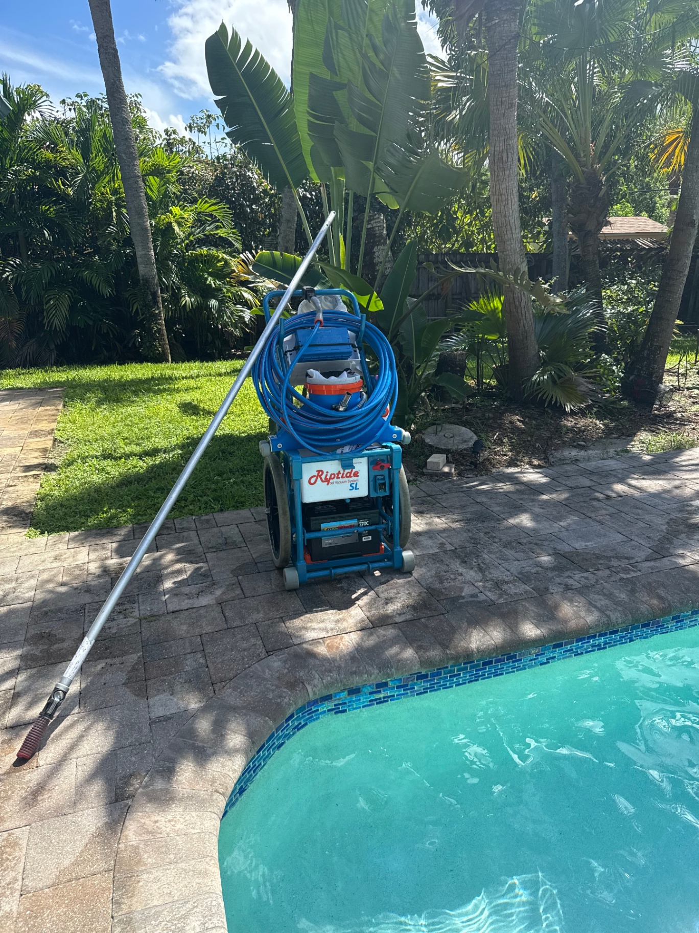Riptide SL vacuum system Riptide SL pool vacuum system and pole staged on a paver deck next to a Palm Beach pool