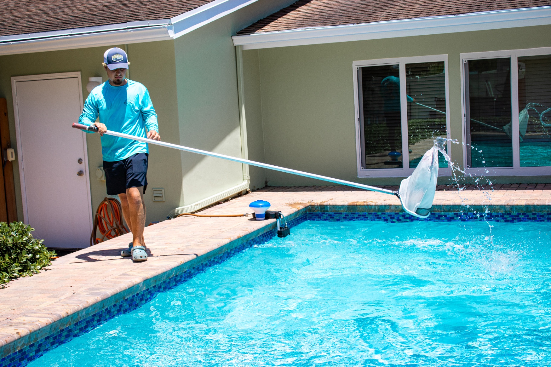 Weekly skim & clean Collegiate Pools technician skimming leaves from a backyard pool in Palm Beach County, FL