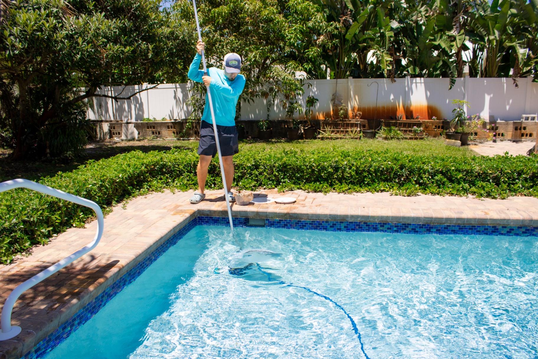 Deep vacuuming a backyard pool Collegiate Pools technician vacuuming a tropical backyard swimming pool in West Palm Beach